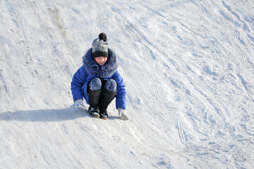 Fototapeta na wymiar The girl squats and descends on her feet on a slippery snow slide.