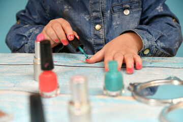 Lipstick, a mirror and other cosmetics near a child who paints his nails with red varnish.