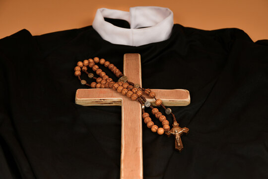 The Catholic cross and rosary lie on the black robe of the priest on a beige background.