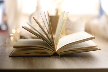 Open book, reading glasses, various candles and vase with flowers. Hygge at home. Selective focus.