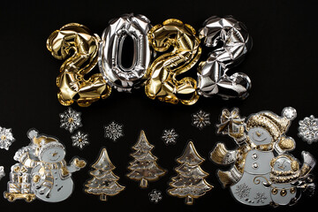 Banner. Happy New Year and Merry Christmas. Balloons made of gold and silver foil with the number 2022 and snowmen on a black background. Flat lay.
