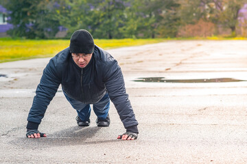 A man performs a classic pectoral exercise outdoors in the rain in the fall. The athlete does...