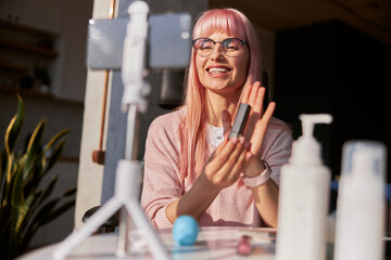 Positive woman blogger with glasses holds lipstick recording video at home