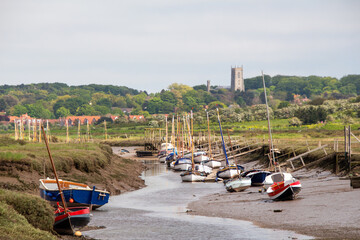 Boats stranded during low tide with Quay and Blakeney village and Church in the background North...