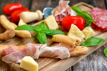 Italian  dried thinly sliced   artisan  pork salami Milano , parmesan cheese, tomatoes   and fresh basil on wooden background .Rustic  home made italian snack.