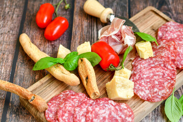 Italian  dried thinly sliced   artisan  pork salami Milano , parmesan cheese, tomatoes   and fresh basil on wooden background .Rustic  home made italian snack.