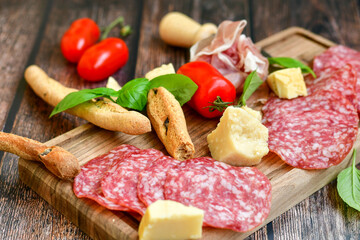 Italian  dried thinly sliced   artisan  pork salami Milano , parmesan cheese, tomatoes   and fresh basil on wooden background .Rustic  home made italian snack.