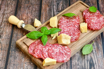 Italian  dried thinly sliced   artisan  pork salami Milano , parmesan cheese, tomatoes   and fresh basil on wooden background .Rustic  home made italian snack.