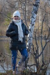 Portrait of a woman against the backdrop of a reservoir. Autumn landscape. Solar warming rays. Warm knitted clothes.