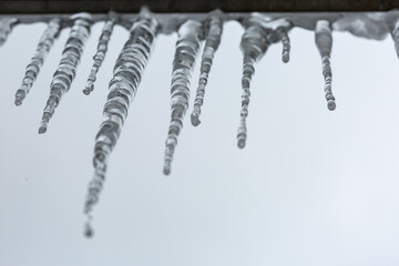 Dangerous icicles hanging from the roof against cloudy sky background