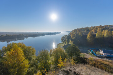 Obraz premium Autumn landscape in the early morning overlooking the river. A wide river and endless expanses of fields. Yellow leaves on trees and bushes are illuminated by the rays of the rising sun.