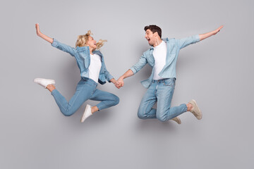 Photo of inspired lover couple jump hold hands wear casual jeans outfit isolated grey color background