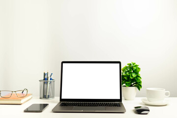 A working concept using technology, notebook, smartphones, devices. Blank white screen laptop on a white table in the office. Copy space on upper for design or text, Closeup, Gray, and blur background