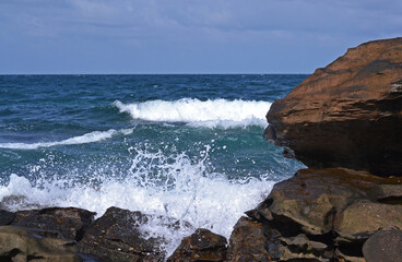 View from the rocky coast to the sea with splashes and white sea foam