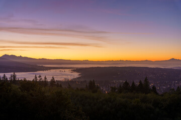 Condominiums peeking through carpet of cloud (inversion)  over Fraser Valley at dawn with mountains in silhouette as backdrop.