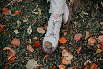 Fototapeta premium Legs of a girl in white shoes on a background of grass and colorful autumn leaves