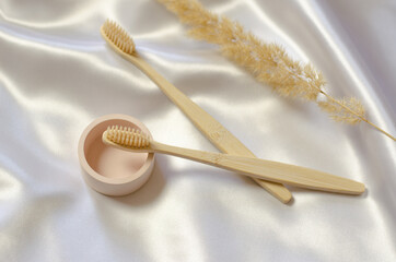 Two wooden toothbrushes and a sprig of pampas grass on a silk cloth.