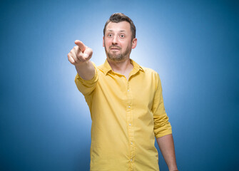 Prank man laughing at you and pointing with finger to the camera over blue background, dresses in...