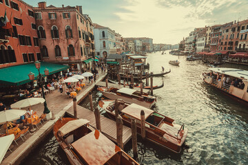 Fototapeta na wymiar Evening light over Venice with bars, water taxi boats, travelers and Grand Canal. Historical buildings and many people on streets of ancient italian city. Cultural landscape with water canals