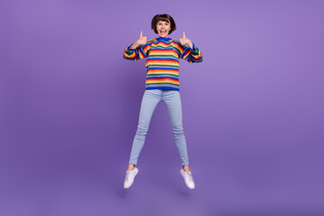 Fototapeta na wymiar Photo of cute lady jump raise thumbs up give feedback wear striped sweater jeans shoes isolated violet color background