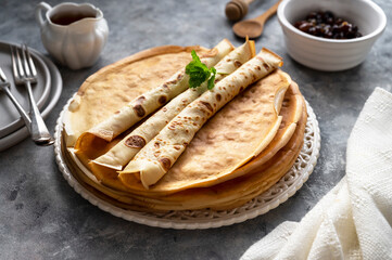 Homemade pancakes or crepes with jam and honey, on grey background.