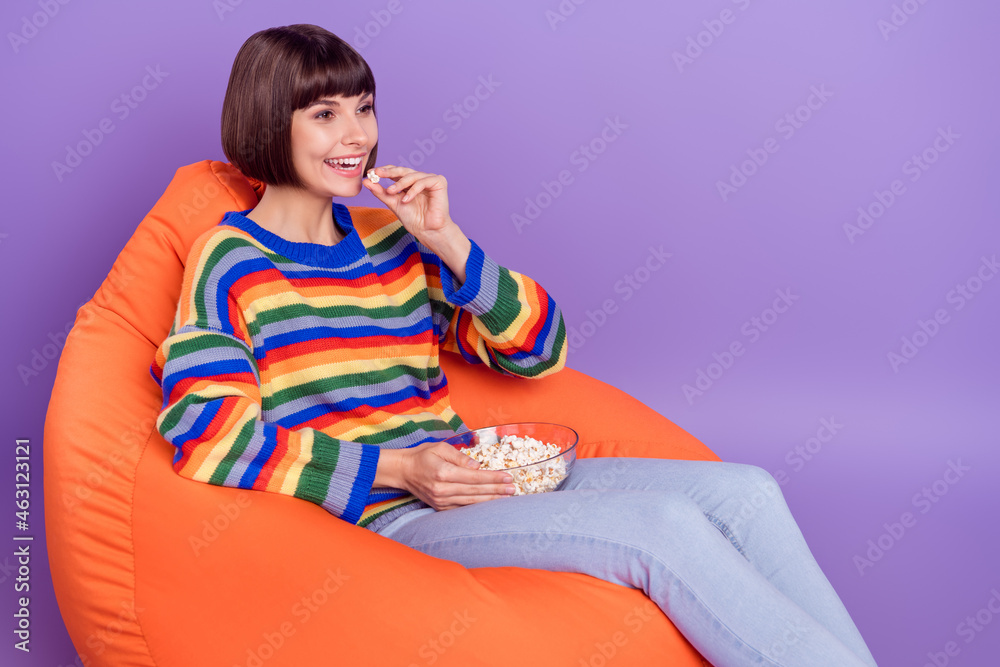 Wall mural Photo of positive lady sit beanbag eat popcorn enjoy cinema wear striped pullover isolated violet color background