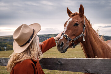 Woman with cowboy hat with her thoroughbred horse at ranch. Cowgirl in animal farm. Friendship between people and horse