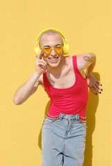 Smiling young non-binary person listening to music with wireless yellow headphones outdoors.