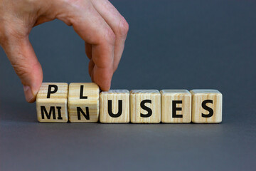 Pluses and minuses symbol. Businessman turns wooden cubes and changes the word 'minuses' to 'pluses'. Beautiful grey table, grey background. Business, pluses and minuses concept, copy space.