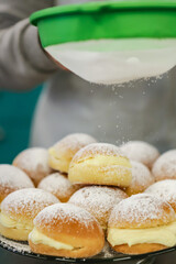 Known in Brazil as a dream, it is a kind of sweet bread filled with cream and covered with sugar that is being placed on top of the sweets in a sieve.
