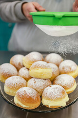 Known in Brazil as a dream, it is a kind of sweet bread filled with cream and covered with sugar that is being placed on top of the sweets in a sieve.
