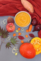 Creamy squash soup, pumpkin, apple, baby carrots, leek and red onion on a table. Top view photo of autumn food. Balanced diet concept. 