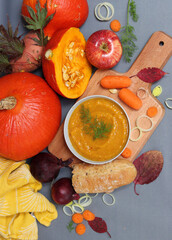 Bowl of hot pumpkin soup, seasonal vegetables and fruits on a table. Vegetarian meal close up. Healthy eating concept. 