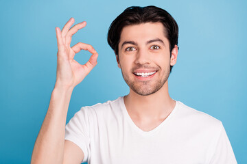 Photo of positive reliable guy show okey sign approve excellent choice wear white t-shirt isolated blue color background