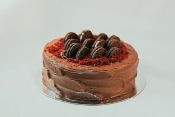 Delicious rich dark cake with Oreo on top on white background. Beautiful tasty sweet dessert with multiple layers decorated with cookies and red velvet frosting