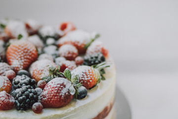 Delicious white cake with natural fruits and white powder on top on white background. Beautiful tasty sweet dessert with multiple layers decorated with strawberry raspberry blueberry and blackberry