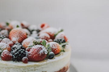Delicious white cake with natural fruits and white powder on top on white background. Beautiful tasty sweet dessert with multiple layers decorated with strawberry raspberry blueberry and blackberry