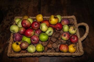 Wicker vintage basket full of apples and walnuts on a brown table , still life, top view