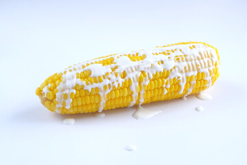 corn on the cob topped with cream or milk on a white background
