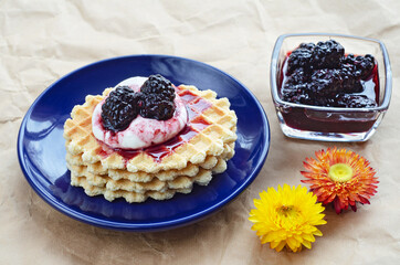Waffle cake with sour cream and candied blackberries on a plate. Crumpled paper background and dried flowers