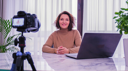 Smiling woman recording her video blog. Woman blogger videotapes her vlog at home.  Adult woman...