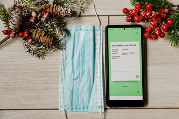 Phone with electronic Covid Vaccination Certificate and medical mask on Christmas background