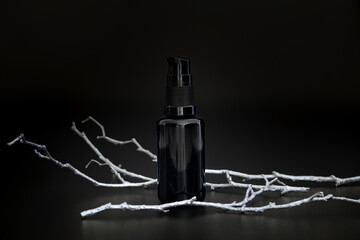 Black unbranded cosmetic serum with silver tree branch. Skin care product presentation on the black...