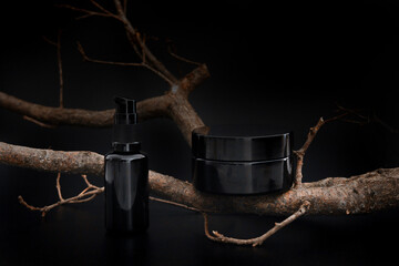 Black unbranded cosmetic cream jar and serum with tree branch. Skin care product presentation on...