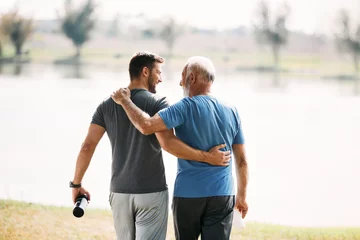 Foto op Plexiglas Rear view of athletic father and son talk while walking embraced by the lake. © Drazen