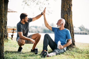 Happy senor athlete and his son greet with high-five after sports training in nature. - Powered by Adobe