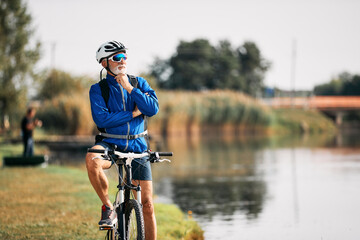 Fototapeta premium Senior cyclist enjoys the view while taking break by the lake. Copy space.