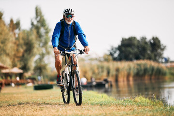 Senior athlete rides mountain bike by the river in nature. Copy space.