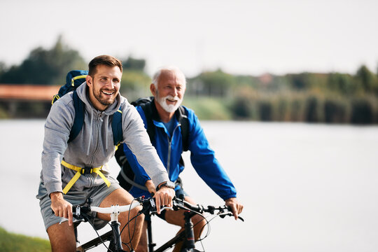 Happy athletic man enjoys in cycling with his senior father by the river. Copy space.