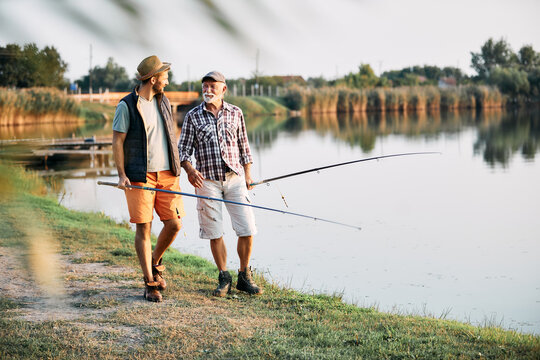 Smiling senior father talk to his son while fishing on the river.